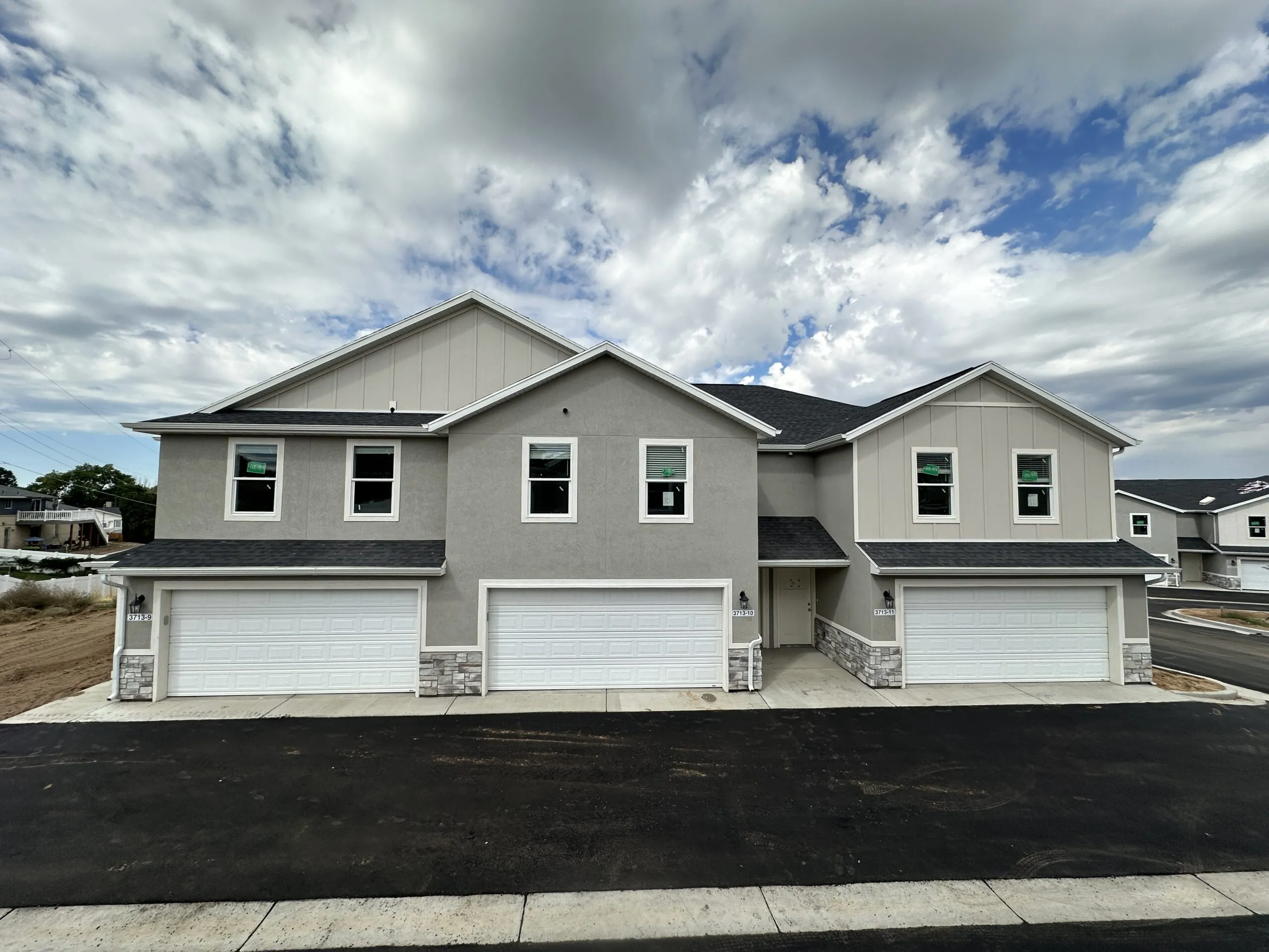 Modern duplex with gray siding and white trim, featuring two garages and a paved driveway. The sky is cloudy, creating a serene atmosphere.